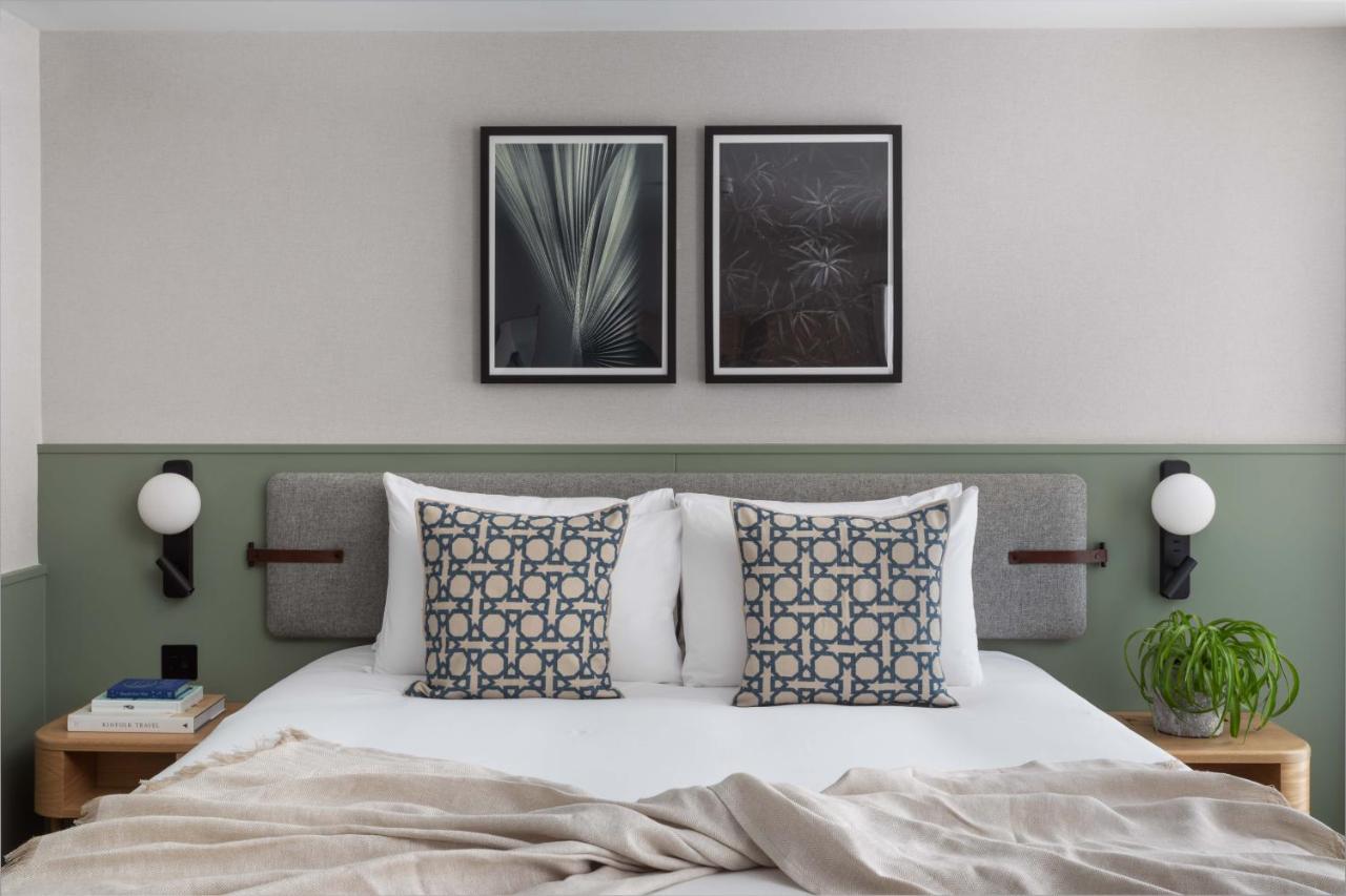 Inhabit Queen'S Gardens, A Member Of Design Hotels London Eksteriør billede The photo shows a modern and stylish bedroom featuring a cozy bed with two decorative pillows at the headboard. The bed is neatly made with a light, soft blanket draped over it. Above the bed, there are two framed artworks that add a touch of eleganc