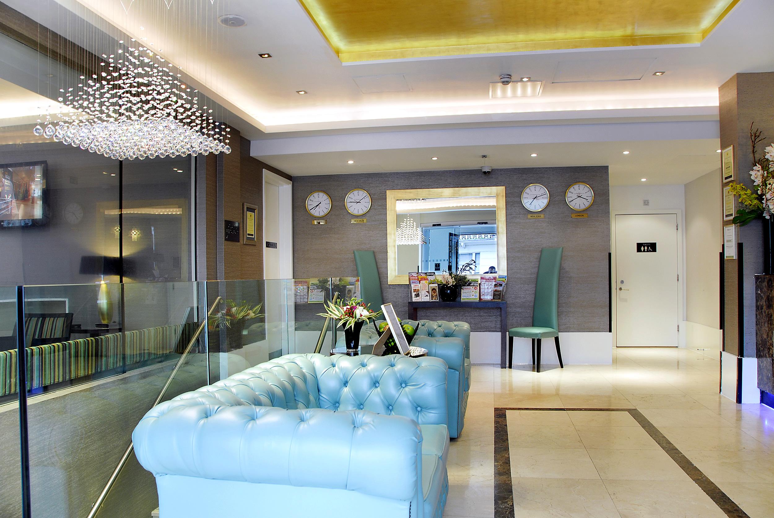 Inhabit Queen'S Gardens, A Member Of Design Hotels London Eksteriør billede The photo depicts an elegant hotel lobby. It features a stylish light blue chesterfield sofa, a modern glass partition, and a reception desk in the background. There are wall clocks displaying different times, adding an international touch. The lobby